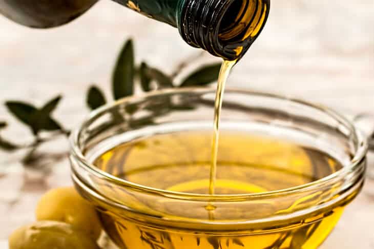 Olive oil being poured from a bottle into a glass. Olive branch in background