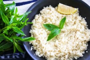 Cauliflower rice in black frypan with a wedge of lemon, a few mint leaves and a bunch of mint