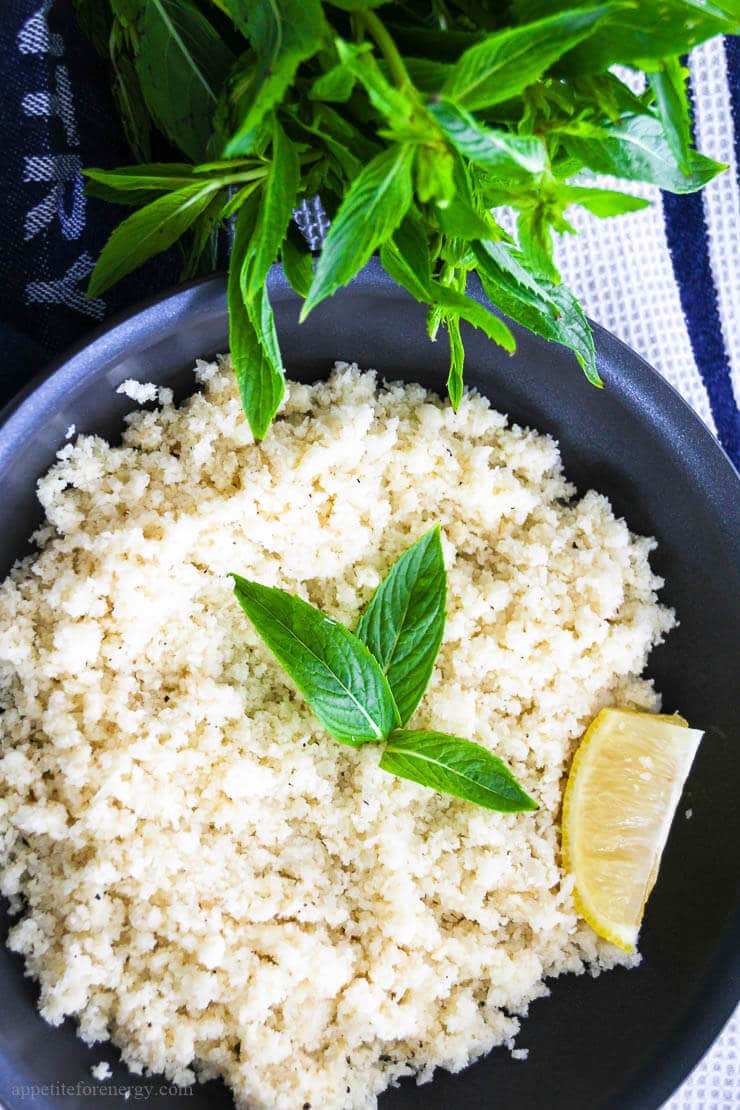 Cauliflower rice in black frypan with a wedge of lemon, a few mint leaves and a bunch of mint next to the pan