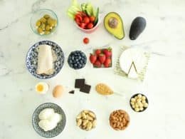 Olives, tomatoes, avocado, brie, nuts,peanut butter, dark chocolate, eggs, turkey on a marble benchtop