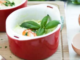 Baked eggs in a red ramekin with basil on top