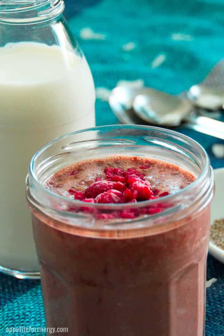 Chocolate chia pudding in a jar sprinkled with raspberries. A bottle of milk, chia seeds, spoons in background.
