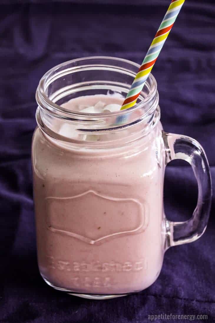 Raspberry Keto Protein Shake in a glass mason jar with handle and colorful stripey straw