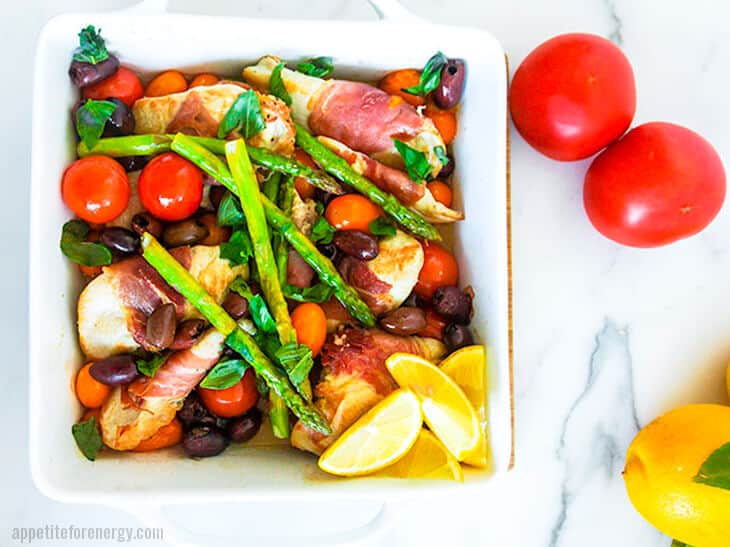 30 Minute Low-Carb Summer Chicken Tray Bake in a baking dish with tomatoes and lemons nearby