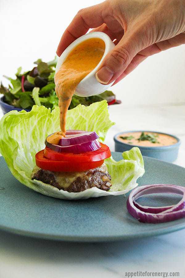 Pouring Chipotle Mayo onto a Low-Carb Burgers
