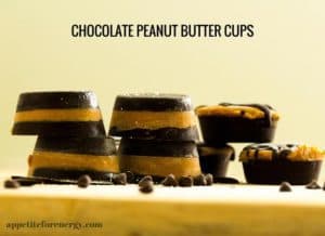 Chocolate peanut butter cups stacked up on a wooden board with choc chips scattered around