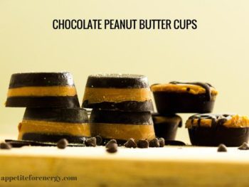 Chocolate peanut butter cups stacked up on a wooden board with choc chips scattered around