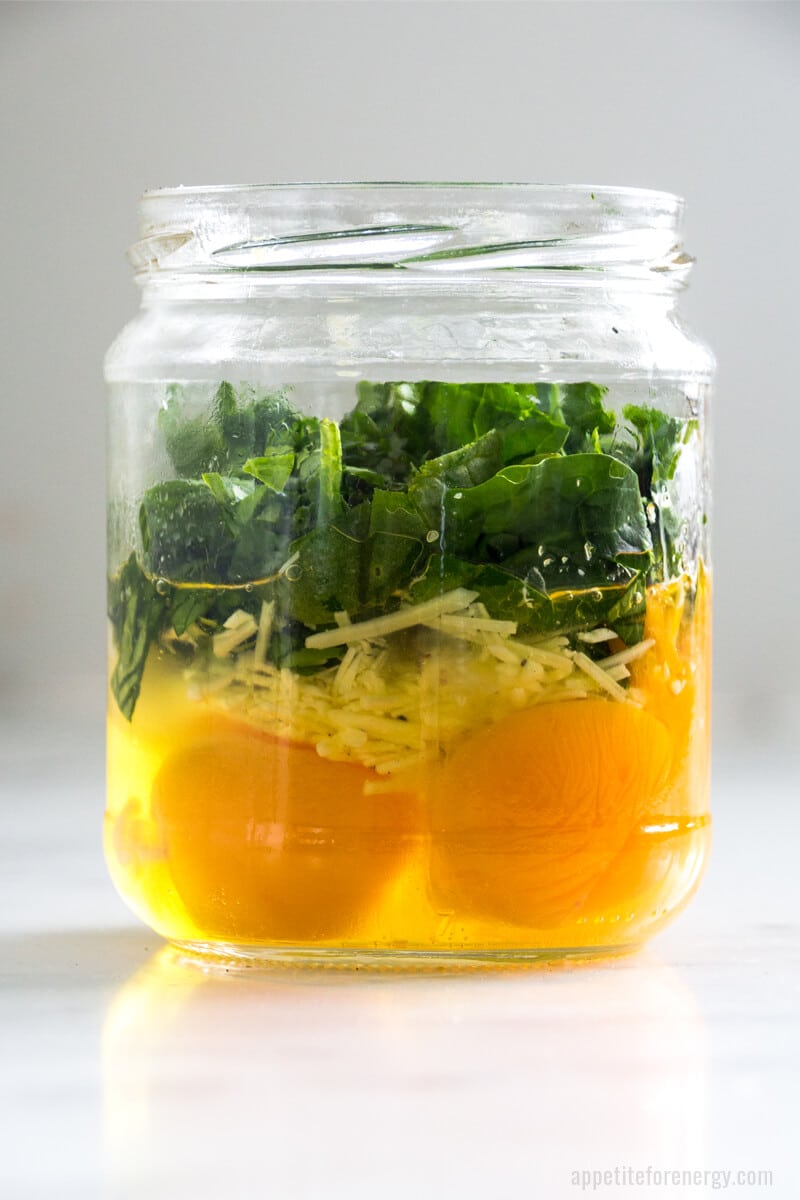Side view of mason jar with ingredients layered ready for cooking - raw eggs, grated cheese, spinach
