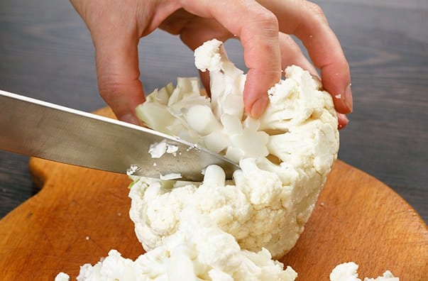 Cutting the cauliflower into florets using the tip of a sharp knife on a wooden board