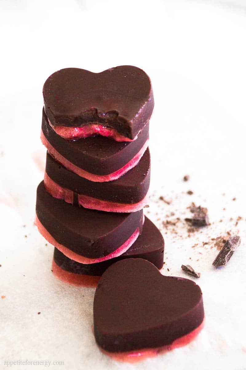 A stack of heart shaped, layered Mint Chocolate Strawberry Fat Bombs. The top fat bomb has a bite taken out of it.