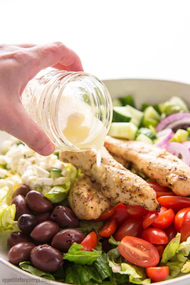 Pouring the lemon vinaigrette from a jar over the Grilled Chicken Salad. 