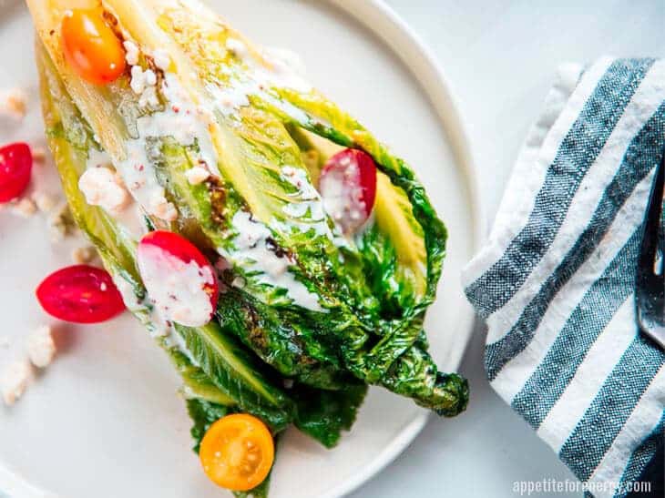 grilled romaine lettuces on a white plate scattered with grape tomatoes and vinaigrette dressing