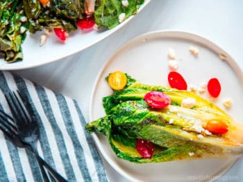 Grilled Romaine on a white plate topped with tomatoes, vinaigrette with a cloth and knife and fork beside