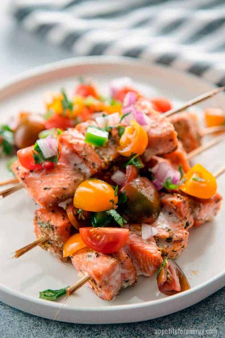 Grilled Salmon Kabobs on a white plate with tomato salsa and fresh herbs scattered on top