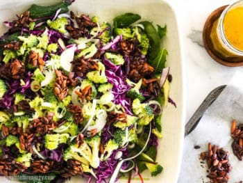 Crunchy Broccoli Slaw in a white serving bowl with nut clusters and dressing in a jar