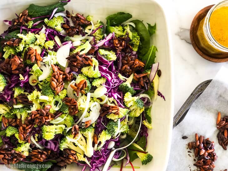 Crunchy Broccoli Slaw in a white serving bowl with nut clusters and dressing in a jar