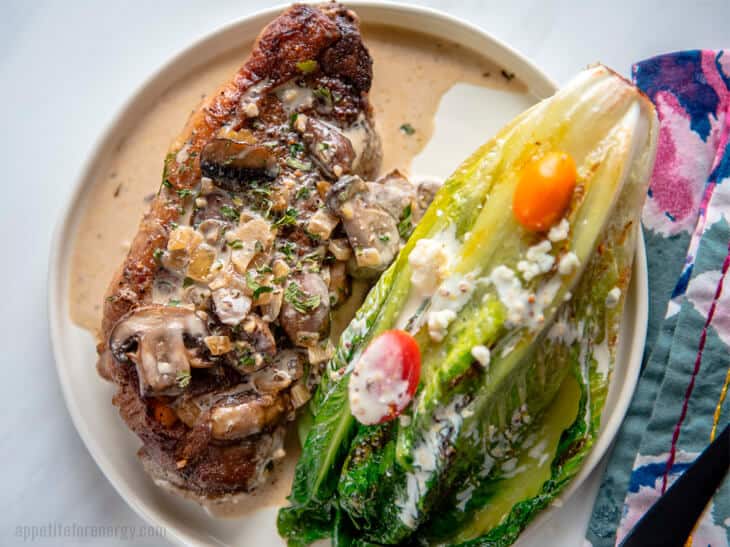 Skillet Strip Steak with Mushroom Sauce on a white plate with grilled romaine lettuce