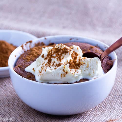 Pumpkin Spice Keto Mug Cake with whipped cream in a small bowl with spoon