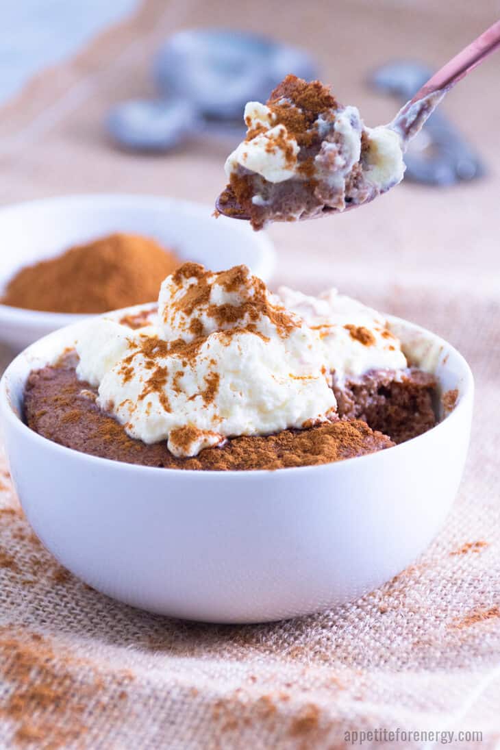 A spoonful of Pumpkin Spice Mug Cake with whipped cream and the cake in a bowl