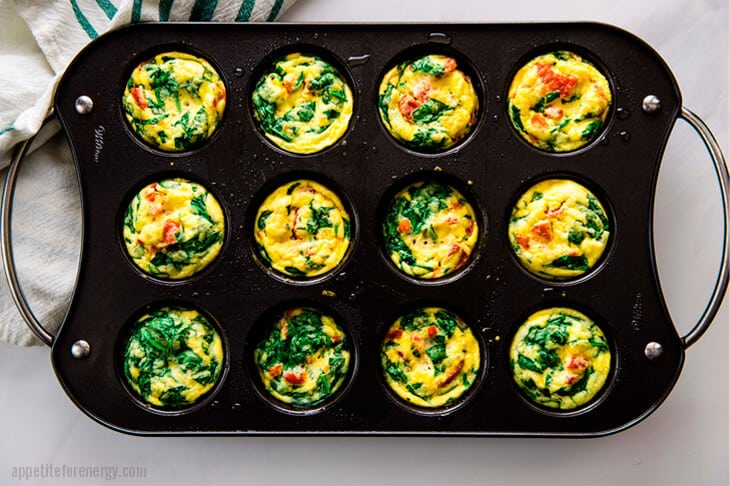 Overhead shot of 12 Spinach and Red Pepper Egg Bites in a muffin tin, just cooked