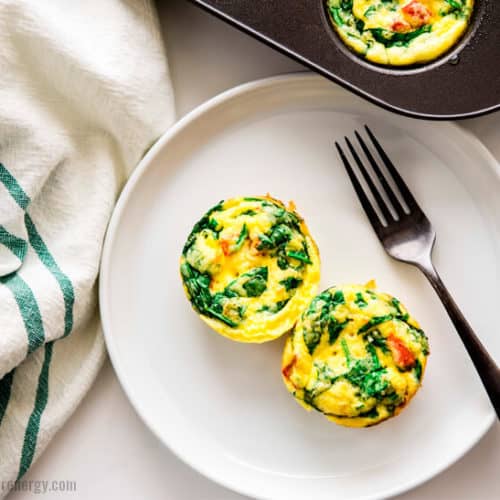 Overhead shot of 2 Spinach and Red Pepper Egg Bites on a plate with a fork and more egg bites in the muffin tin