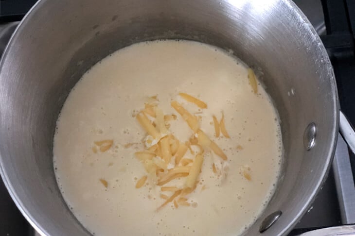 Adding shredded cheese to the saucepan with the mac and cheese sauce