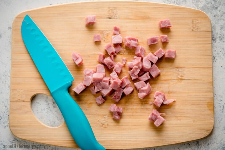 Chopped leftover ham on a wooden board with blue chefs knife