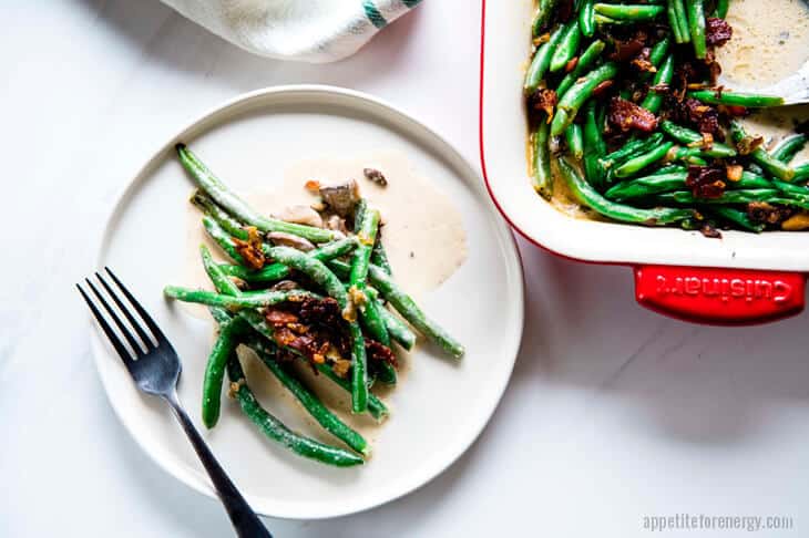 Keto Sautéed Green Beans with Bacon Cream Sauce on a white plate with fork and serving dish behind