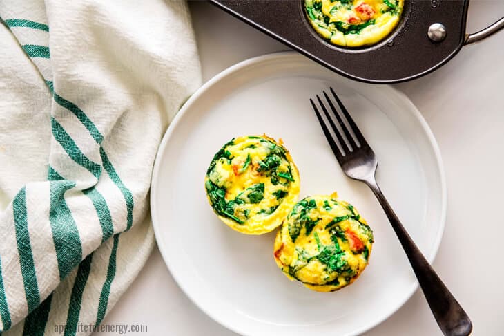 Overhead shot of 2 Spinach and Red Pepper Egg Bites on a plate with a fork and more egg bites in the muffin tin
