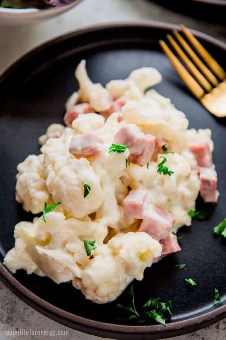 Close up of Keto Cauliflower Mac and Cheese with Ham on a black plate with gold fork
