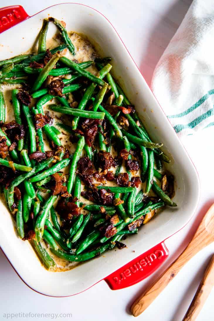 Keto Sautéed Green Beans with Bacon Cream Sauce in a white serving dish on the dining table with napkin, wooden spoon