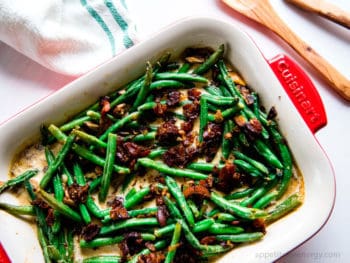 Keto Sautéed Green Beans with Bacon Cream Sauce in a white serving dish on the dining table with napkin, wooden spoon