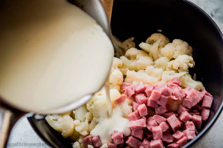 Pouring cheese sauce from ladle onto Cauliflower and Ham