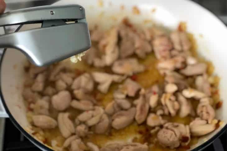 A garlic crusher, mincing garlic directly onto chicken in pan