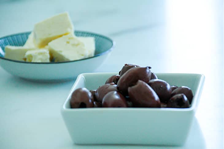 Kalamata olives in a white dish and cubes of feta cheese in another dish