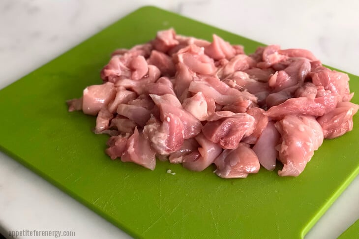 Chicken chopped into bite sized pieces on a green chopping board