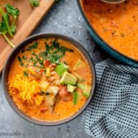 Overhead shot of Chicken Taco Soup in grey bowl with ladle, avocado and tomatoes