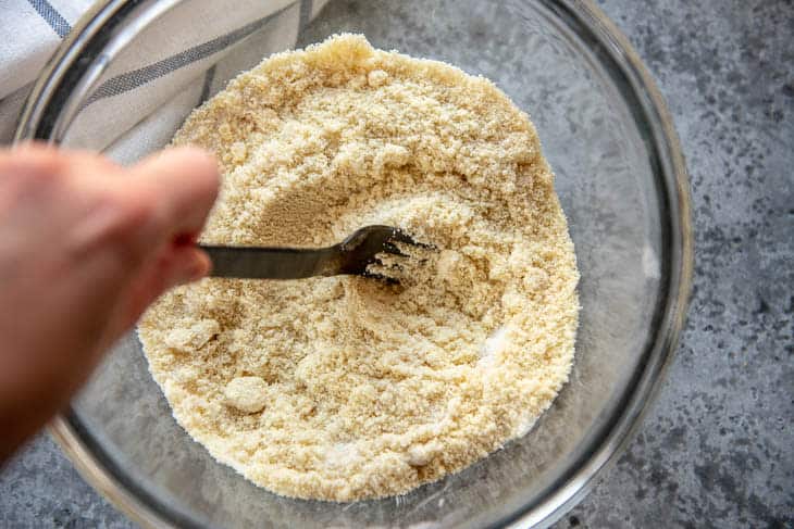 A hand using fork to stir together almond flour and sweetener