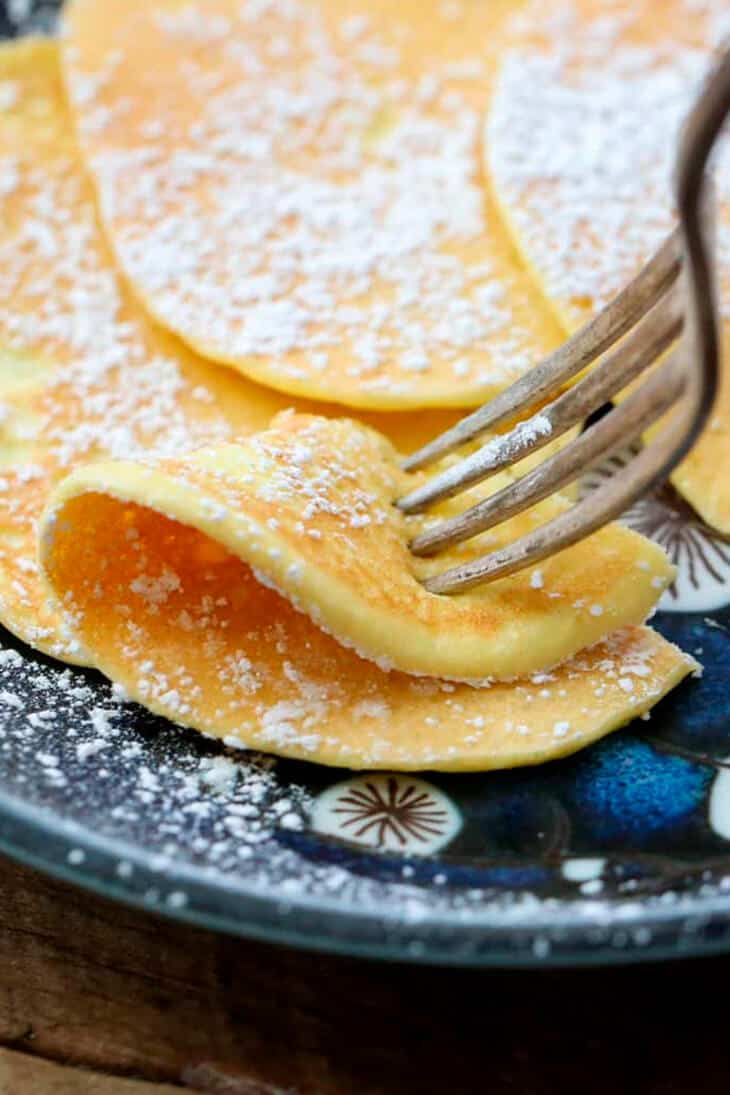 Close up of a fork digging into a thin, crepe style pancake topped with powdered erythritol