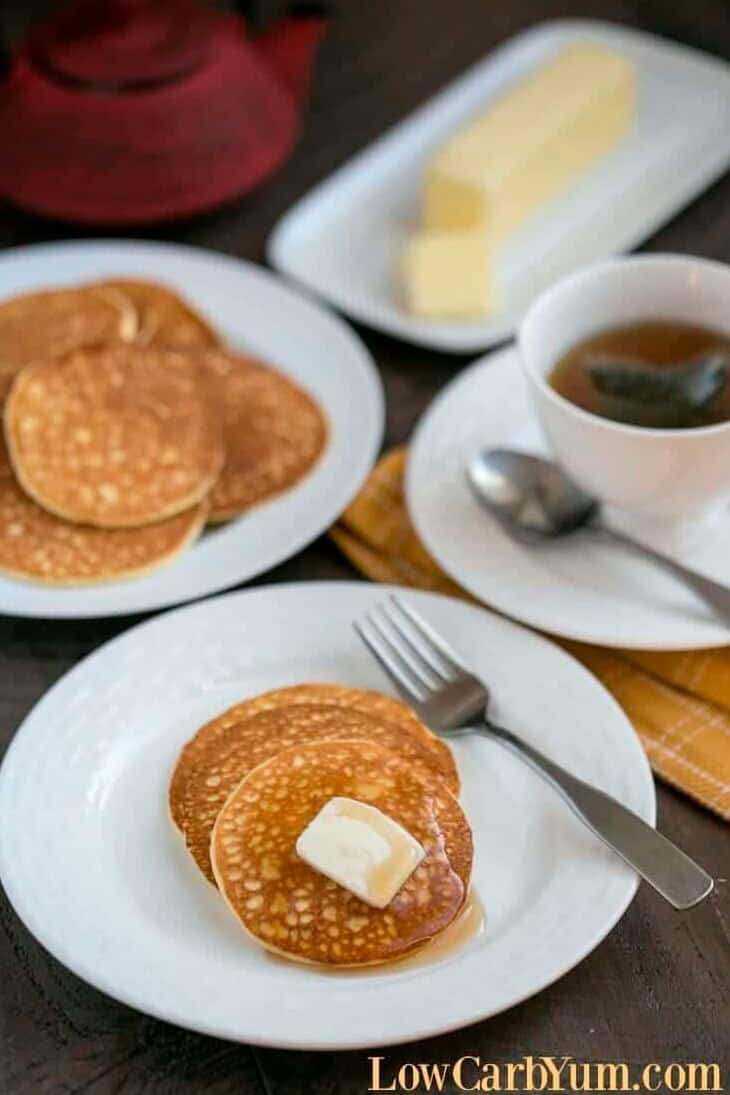 A few pancakes on a white plate with butter on top and a cup of black coffee