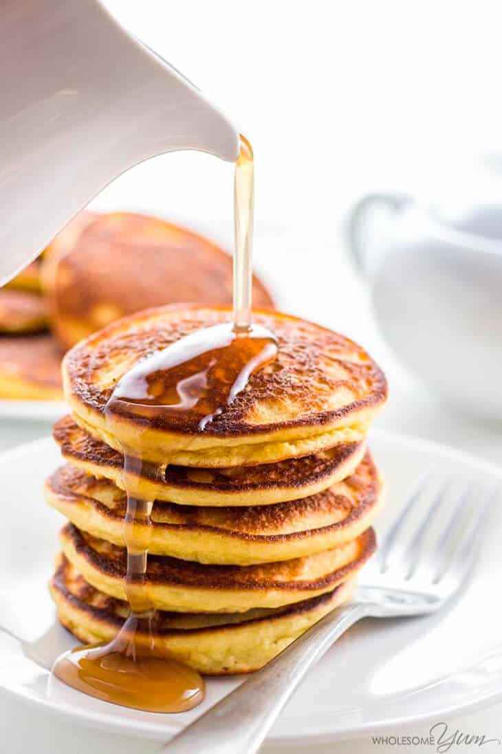 A stack of golden pancakes with low-carb pancake syrup being poured over the top