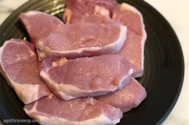 uncooked boneless pork loin chops stacked on a black plate