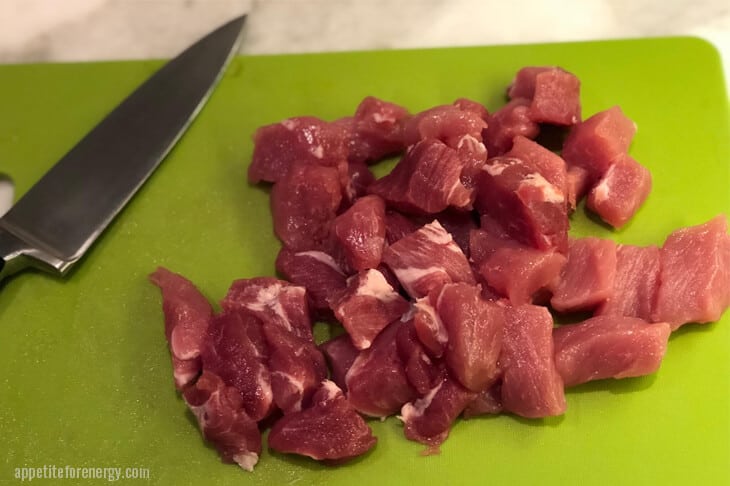 pork cut into bit sized pieces on a green plastic cuttign board with sharp knife