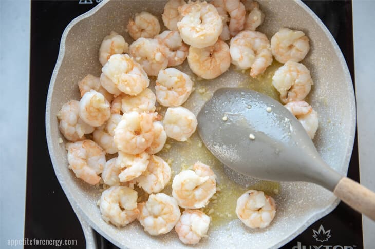 Cooking the garlic and shrimp in a white skillet with a metal spoon