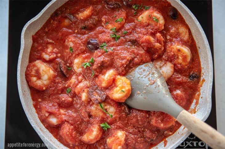 Cooking the shrimp in a large white skillet with tomatoes, olives, garlic