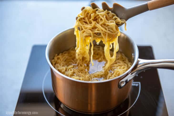 Shirataki konjac noodles being lifted out of boiling water in saucepan with pasta ladle