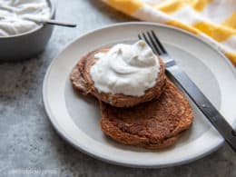 Chocolate Protein Pancakes on a white plate smothered in cream, with a fork