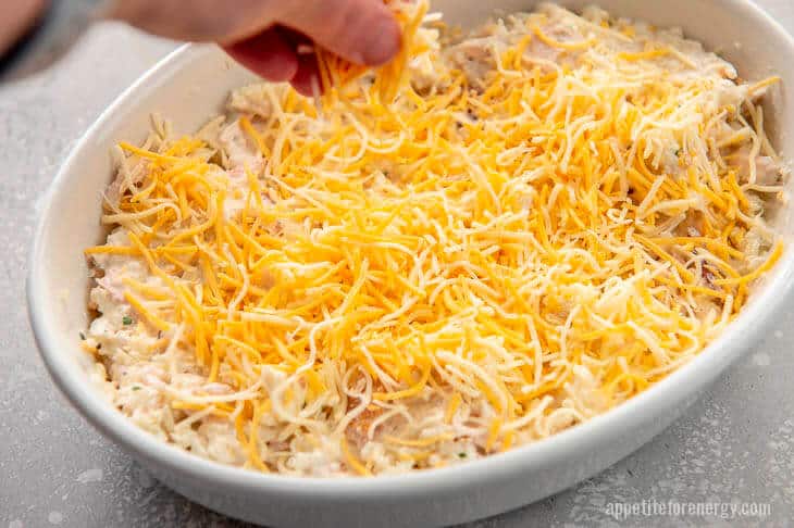 Adding cheese to Ingredients mixed in baking dish for keto cauliflower casserole