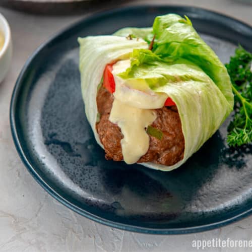 Lettuce wrapped pork burger with sauce drizzled over on blue plate